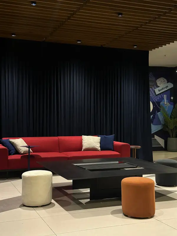 A lounge with a red sofa, a low black table and round stools in front of a navy curtain.