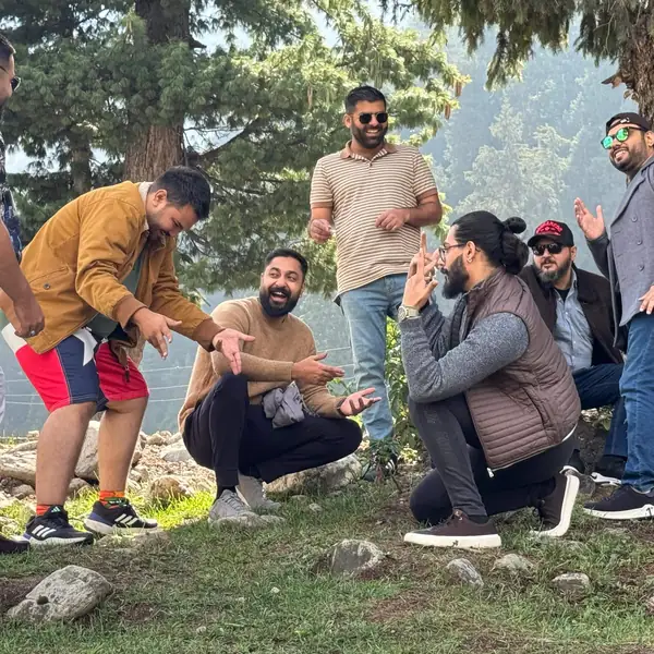 Colleagues laughing together under a pine tree on a team trip.